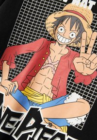 L'image présente un personnage de dessin animé avec des cheveux noirs, portant une veste rouge et un chapeau de paille, sur un fond en grille noire, avec du texte lisible.