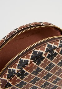 Braune und schwarze gemusterte Tasche in runder Form, mit goldenem Reißverschluss und strukturiertem Außenmaterial. Das Innenfutter besteht aus glattem braunem Material.