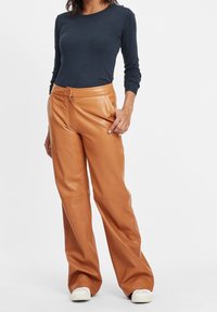 Bruna läderbyxor med rak benmodell, med dragkedja fram och detaljer i midjan. Matchas med en mörkblå långärmad topp.