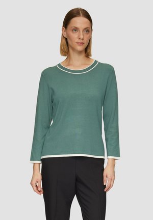 Chemise verte à manches longues avec un liseré blanc autour de l'encolure ronde et des manches, présentant une coupe décontractée et une texture lisse.