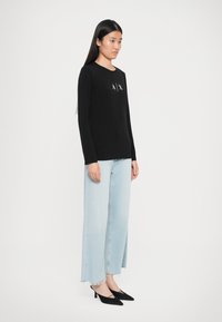Musthave mustaelari, sisaldab "A|X" logo rinnal, koos helesiniste laiaribadega teksade ja mustade terava ninaga kontsakingadega.