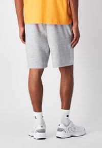 Graue Baumwollshorts mit einem lockeren Schnitt und einem elastischen Bund. Kombiniert mit weißen Socken und Sportschuhen. Schlichtes Design, keine Muster.