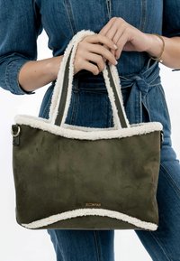 Borsa a tote verde oliva con un morbido bordo in pile crema, doppi manici e un tessuto testurizzato. Presenta un dettaglio di branding dorato sulla parte frontale.