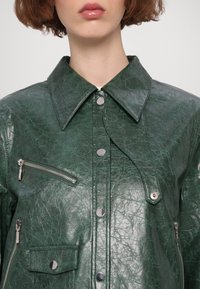 Zielona skórzana kurtka o pomarszczonej fakturze, z dużym kołnierzem, srebrnymi elementami i kieszeniami na zamek. Wyposażona w zamki błyskawiczne i zatrzaski.
