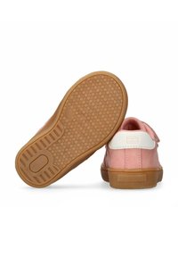 Scarpe in suede rosa con un accento bianco sul tacco, cinturino in velcro e suola in gomma testurizzata con un motivo di presa circolare.