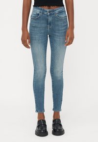 Tanke modre jeans iz denima, z srednjim pasom, petimi žepi in rahlim bledenjem. V kombinaciji z črnimi loafers.
