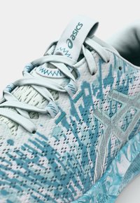 Baskets de sport bleu clair avec un dessus texturé, des motifs abstraits, des sections en mesh et une languette avec logo. Design minimaliste.