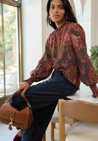 Multicolored floral blouse with long sleeves and ruffled cuffs, paired with dark wide-leg pants. Brown handbag with gold hardware detail.