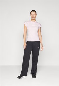 T-shirt de manga curta rosa claro com logo branco, combinada com calças de treino largas pretas com um pequeno logo em branco. Sapatos de desporto pretos.