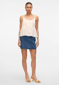 Crèmefarvet, let peplum top med tynde stropper, parret med en mørk denim mini nederdel og gule hæle sandaler.