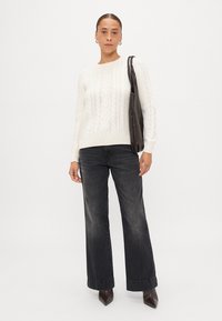 Krém színű, cable-knit pulóver kerek nyakkivágással, széles szárú fekete farmernadrággal párosítva. Kiegészítők közé tartozik egy sötét kézitáska és karika fülbevalók.