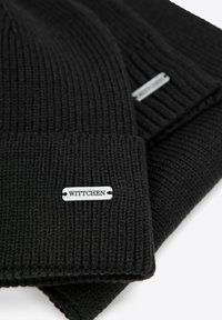 Czarne dziergane czapki z miękkiego materiału, z odwiniętym mankietem i srebrną metką z logo "WITTCHEN" po boku.