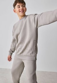 Grå sweatshirt og matchende bukser lavet af blødt stof. Sweatshirten har et præget logo og ribbet manchetter. Enkel, afslappet pasform.