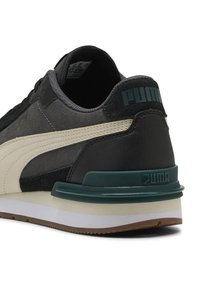 Graue und schwarze Puma-Sneaker mit beigem Streifen, türkisfarbenem Fersenstütze, weißer Zwischensohle und braunem Außensohle, von der Rückseite in schräger Ansicht gezeigt.