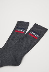 Des chaussettes en coton grises de type crew avec une texture côtelée, arborant le logo contrastant de Levi's en rouge et bleu marine sur le haut.