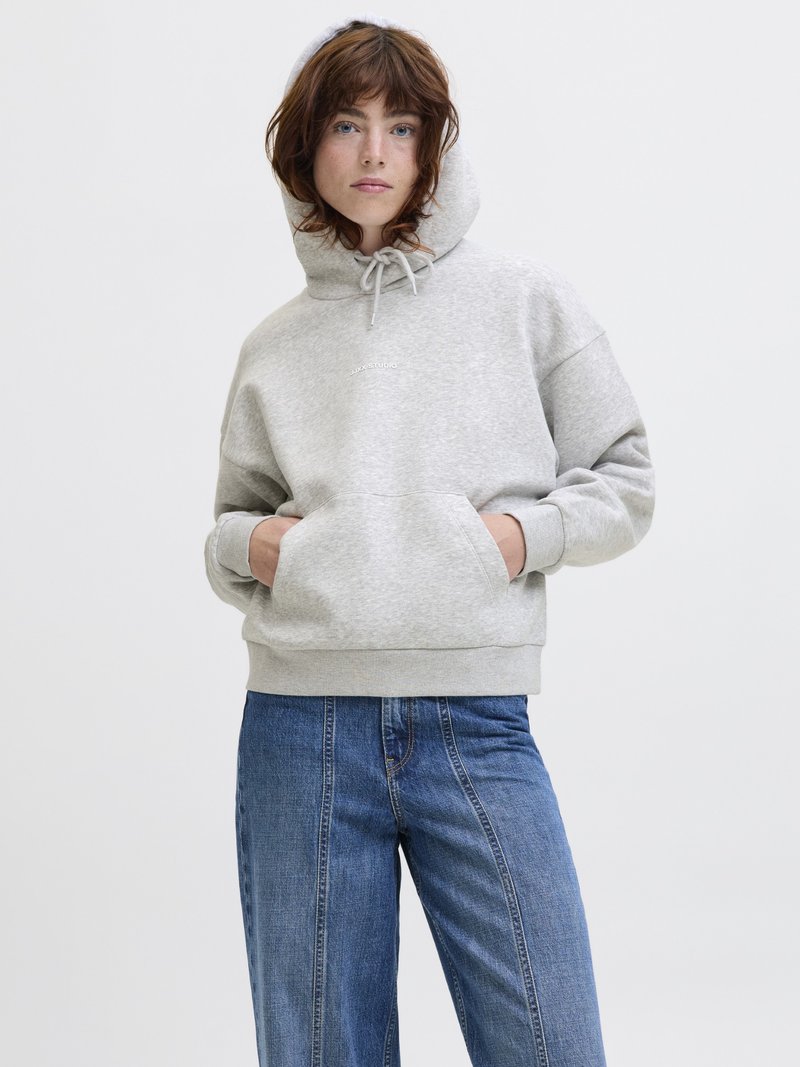 Moleton cinza de algodão com um bolso frontal, capuz com cordão e logotipo bordado no peito, combinado com jeans azuis de perna larga com costuras verticais.