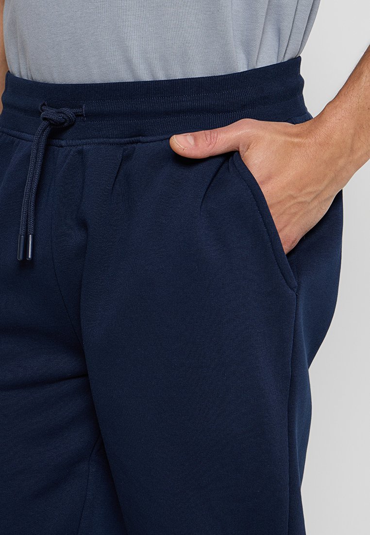 Pantaloni della tuta blu navy con cintura regolabile, tasche laterali e texture morbida. Vista ravvicinata del tessuto e mano nella tasca.