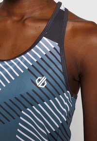 Urheilutoppi syvänvihreänä, jossa vinoraitoja mustana ja valkoisena. Mallissa on takaa kapeampi leikkaus ja nurkassa logo. Sileä pinta.