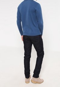 Camisa de manga larga azul combinada con jeans de mezclilla oscuros y botines beige claro, con un diseño sencillo y texturas suaves.