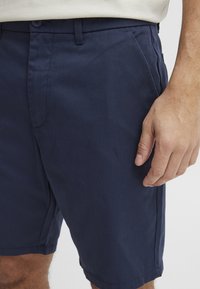 Navy blue shorts in a lightweight fabric with a smooth texture. Features a flat front, two side pockets, and a button closure.