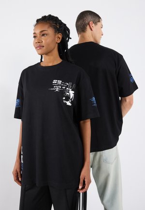 T-shirt noir surdimensionné en coton, avec des imprimés graphiques blancs et bleus sur le devant et les manches. Manches courtes, design col rond.