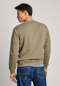 Sudadera color caqui con cuello redondo, mangas largas y puños acanalados, combinada con jeans azules; textura suave, sin patrones o herrajes visibles.