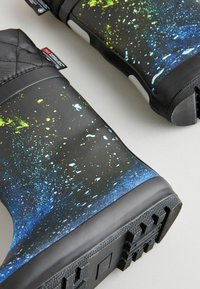 Bottes noires imperméables avec un dessus texturé présentant un motif éclaboussé coloré en vert et bleu. Semelle en caoutchouc avec détails de grip.