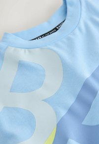 T-shirt bleu clair avec un col rond, présentant de grands motifs graphiques blancs et jaunes. Confectionné dans un tissu doux et lisse avec une coupe décontractée.
