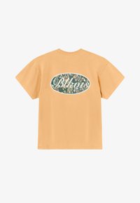 T-shirt à manches courtes, col rond en coton orange clair. Présente un patch ovale à motif floral vert avec des lettres blanches au dos.