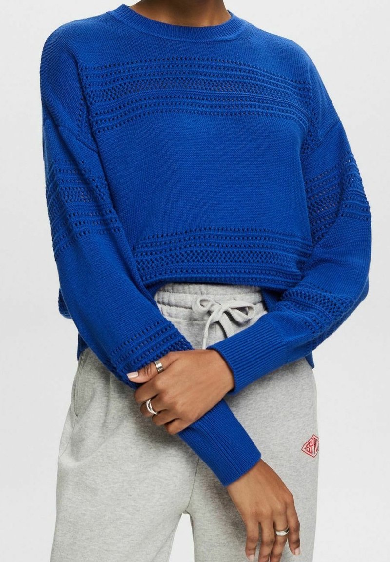 Blaues Strickpullover mit strukturiertem Muster, Rundhalsausschnitt und langen Ärmeln, kombiniert mit hellgrauen Sweatpants mit kleinem Logo.