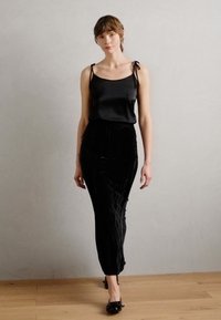 Camisole en satin noir avec des liens aux épaules, associé à une jupe en velours noir fluide ornée de lignes verticales texturées, complétée par des ballerines noires.