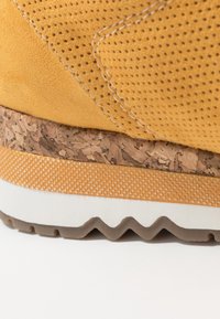 Zapatilla de ante amarilla con detalles perforados, entresuela de corcho y suela de goma texturizada con un patrón en zigzag.