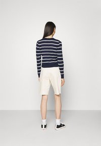 Suéter de rayas azul marino y blanco de manga larga combinado con pantalones cortos blancos hasta la rodilla. Zapatillas con detalles en negro y calcetines blancos.