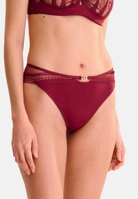 Des culottes bordeaux en tissu lisse avec une finition en dentelle le long de la taille et un petit accent doré au centre devant.