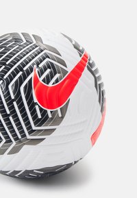 Pallone da calcio Nike con una superficie bianca caratterizzata da motivi geometrici neri, una consistenza texturizzata e un grande logo swoosh rosso Nike.