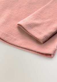 Vaaleanpunainen kangas, jossa on taitettu helma ja pehmeä tekstuuri; huomaamaton ommel viimeistely reunoissa.
