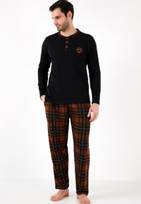 Camisa negra de manga larga con tapeta de botones y acentos de cuadros; pantalones de cuadros marrones con líneas negras, hechos de una tela suave.