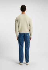 Beige gerippter Pullover mit langen Ärmeln, kombiniert mit blauen Denim-Cargohosen mit mehreren Taschen und einem lockeren Schnitt. Off-white Sneakers.