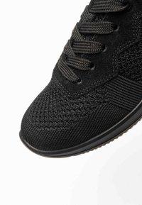 Black athletic shoe toe with textured knit fabric, suede eyelet panel, and black laces on a white background.