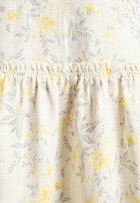 Valkoinen kangas, jossa on keltainen ja harmaa kukkakuosi, ja jossa on rypistetty tekstuuri vyötäröllä. Pehmeä, kevyt materiaali hienoilla yksityiskohdilla.