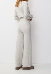 Mono de punto gris claro con cintura ajustada, piernas anchas y mangas largas. Presenta una textura suave y un diseño casual.