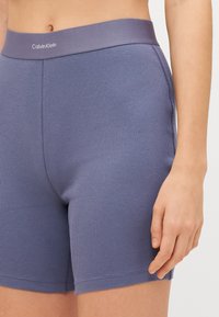 Calvin Klein ribbed stieptas šortos nematā purpura krāsā ar platām jostasvietām, ar gludu tekstūru un pieguļošu dizainu.