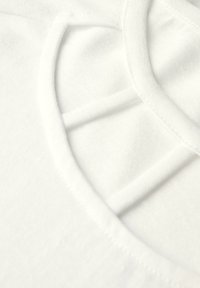 Bílý bavlněný top s širokým výstřihem a strukturovaným křížovým detailem. Měkká textura a viditelné precizní švy.