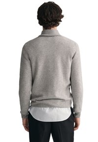 Grauer Strickpullover mit umgeschlagenem Kragen, gerippten Bündchen und Saum, über einem weißen Hemd getragen. Zeigt eine glatte Textur und lockere Passform.