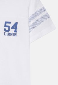 Biela tričko s modrým číslom "54" a nápisom "CHAMPION". Krátke rukávy s modrými bodkovanými pruhmi na pleciach. Bavlnený materiál.