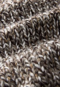 Adīta auduma brūnās, krēmkrāsas un pelēkās toņos ar rupju faktūru, kur redzama diegu vērpšana un smalkas punktētas detaļas.