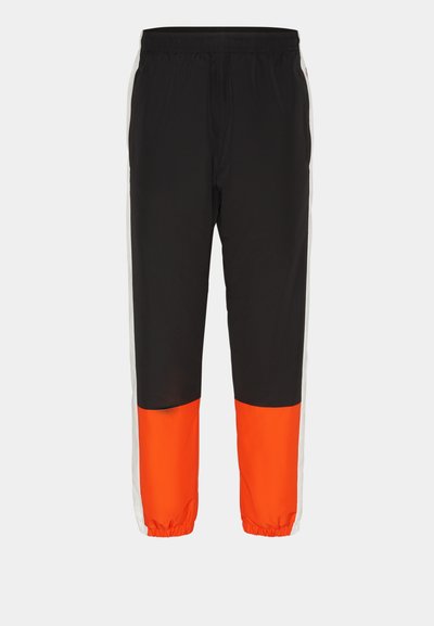 Pantalons de sport noirs avec un large panneau orange en bas et des rayures blanches sur les côtés. Taille élastique et poignets de cheville pour un ajustement réglable.