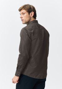 Brown patterned long-sleeve shirt with a button-down collar, featuring a textured fabric and button accents on the cuffs.