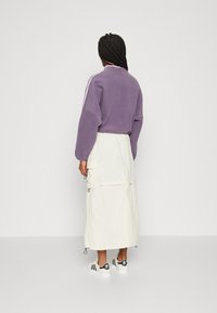 Lila fleece-tröja med sänkta axlar, ihop med en vit lång cargokjol med fickor och dragsko, samt svarta sneakers.