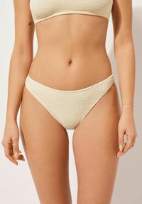 Krämfärgade bikinitrosor gjorda av texturerat tyg med låg midja och sömlös midjeresår. Lämpliga för bad eller strandkläder.